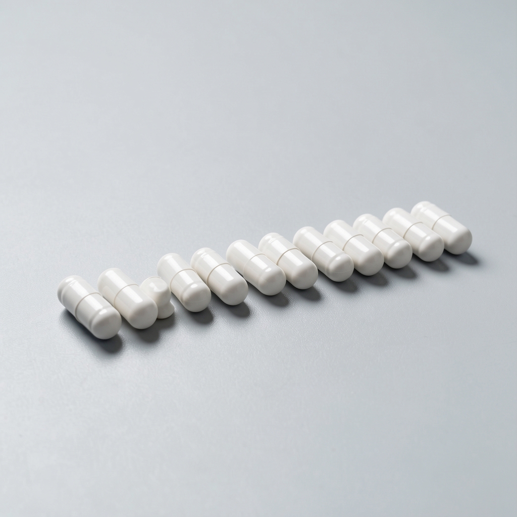 Small white capsules arranged in a precise row on a smooth light-grey surface under controlled bright lighting, composition photography style